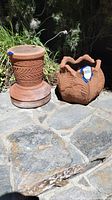 Photo of terracotta pot and plant stand placed on stone patio with plants in background
