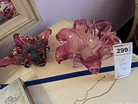 Photo showing two cut glass tinted bowls in pink and purple shades placed on a surface next to a mirror, with a label stating price and description