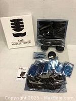 Photo showing the EMS Muscle Toner control unit, multiple gel pads, abdominal and arm muscle toner pads, connecting wires, and instruction booklet laid out with box.