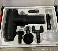 Top box view showing massager and four head attachments inside configuration tray along with USB charging cable.