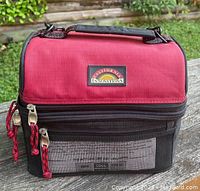 Front view of red and black insulated lunch cooler bag with dual zippers, front mesh pocket, and California Innovations logo patch.