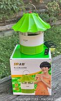 Photo of new green and white electric mosquito killer trapper lamp on table next to its box, showing packaging and device with metal hanging handle.