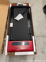 Electric treadmill in packaging showcasing the red base with digital display area, black walking belt, and power cord with accessories.
