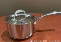 Polished stainless steel 2L saucepan with attached handle and matching lid on wooden surface.