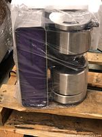 Panasonic NC-ZF1 V coffee maker in violet, wrapped in plastic and placed on wooden pallet, viewed from side showing stainless steel and purple colored parts.