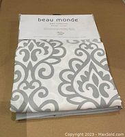 Folded shower curtain with label showing brand Beau Monde and Bath Collection with decorative gray and white pattern