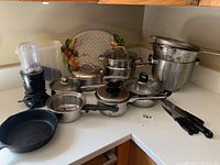 Overview of cooking pots, lids, strainers, cast iron pan, and knives arranged on countertop