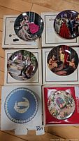 Top view of 6 collector plates depicting Brothers Grimm scenes and one blue Wedgwood plate, all shown with original packaging.