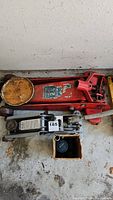 Top view of red hydraulic floor jack and two smaller silver mechanical scissor jacks on floor.