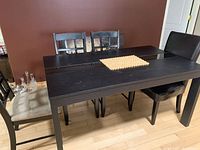 Black rectangular dining table with glass inlay and 6 chairs around it, showing table surface and chair upholstery details.