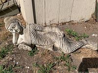 Concrete reclining Buddha garden statue lying on the ground outside. Shows detailed robe folds, peaceful facial expression, and textured hair.