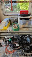 Overview of workspace showing partially used spools of wire, assorted cords, plastic drawers, tape, and workshop supplies on a bench.