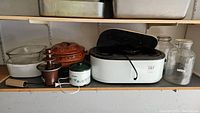 Shelf with electric warmer, glass and ceramic casserole dishes, small chocolate fountain, and glass jars.