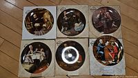 Six Norman Rockwell collector plates in original packaging on wooden floor showing various classic scenes of children and adults