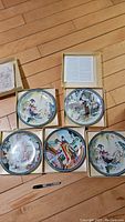 Top view of 5 plates in protective boxes showing various traditional oriental scenes.