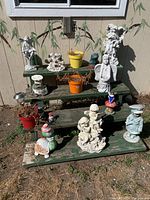Overview of assorted garden decorations arranged on green wooden tiered shelves next to a tan wall with a window