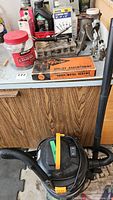 Kubota shop vacuum with hose, and assorted tools and hardware on wooden workbench.