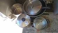 Top view of assortment of stainless steel pots, pans, and bowls showing sizes and lids