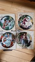 Set of four King And I collector plates laid on wooden floor, each in its original box with visible artwork