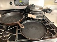 Photo showing two cast iron pans sitting on a stovetop behind a Hamilton Beach waffle iron.