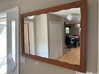Front view of the wall mirror with warm wooden frame showing the irregular wavy edge and reflective glass.