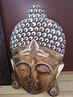 Close-up and front view of large wooden Buddha head carving showing detailed hair and facial features.