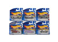 Six Hot Wheels cars in blister card packaging. Top row: silver muscle car, white race car, gray drag car. Bottom row: red classic car, lavender custom car, silver drag car. Packaging has Hot Wheels logo and blue background.