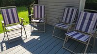 Four folding outdoor camping chairs arranged on a wooden deck with beige metal frames and blue and white striped cushions.
