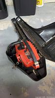 Side view of the chainsaw inside black plastic chain cover showing orange body and chain.