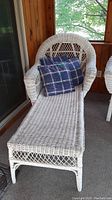 Wicker chaise lounge with three plaid cushions on porch, side angle view showing armrest and seat