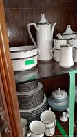 Cabinet view showing stacked plates, pots, creamer, sugar bowl, serving bowls