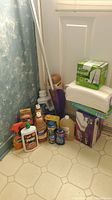 Photo showing assorted cleaning bottles including Pledge spray, wood cleaner, Dutch Boy Amish Wood Milk, Finish dishwasher products, and liquid floor cleaner with Swiffer WetJet and mop sticks in the background.