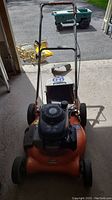 Front view of the orange gas-powered lawn mower with grass catcher attached.