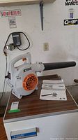 White and orange Stihl BG 50 gas leaf blower on a table with owner's manuals beside it.