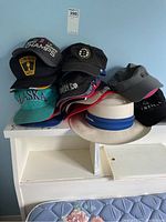 Photo of assorted hats stacked on white shelf including sports teams and a bucket hat