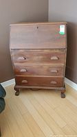 Full front view of the closed vintage drop down secretary desk, showing three drawers with carved wooden handles and claw-foot legs.