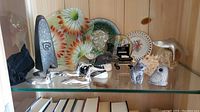 Wide view of shelf containing four silver Hoselton loon figurines, soapstone animal carvings, and multiple decorative plates with floral patterns
