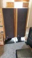 Both tower speakers with grilles installed, showing wood side panels and metal pedestal bases