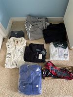 Lot of men's clothes including shirts, track pants, sweaters, and ties arranged on floor