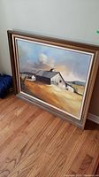 Full view of framed canvas painting leaning against wall, showing barn landscape and frame.
