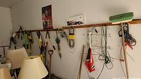 Tools hanging on garage wall including brooms, shovels, loppers, and cords