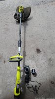 Full view of Ryobi cordless string trimmer unit with battery, charger, and extra line spools laid out on concrete.