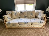 Front view of three-seat sofa with light tan bamboo or rattan frame and beige floral cushions showing overall condition and design.