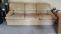 Full front view of the beige three-seater leather sofa on carpeted floor against a wall showing all three seat positions