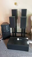 Photo showing overall setup with four satellite speakers on stands, center channel speaker, and subwoofer in a room setting on carpeted floor