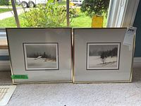 Two framed watercolour paintings by Jack Reed displayed side by side on a windowsill, showing winter rural landscape scenes with snow and trees.