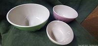 Three nesting ceramic bowls of different sizes and colors placed on a green cloth background. The bowls are displayed loose to show size variation.