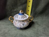 Porcelain sugar bowl with lid, detailed with gold floral patterns, blue base, and gold handles. The photo includes a measuring tape showing about 3 inches tall with lid on.