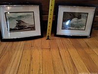 Lot of two framed coastal art prints on wooden floor with measuring tape for scale.