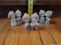 Front view of three Precious Moments figurines on wooden floor, a tape measure behind them shows their height around 2-3 inches.